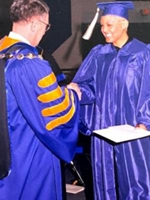 woman in graduation robe holding a degree and shaking hands with man in academic robe